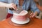 A lovely girl making a cake in a bakery. The girl smoothes the cream on the cake. White cake on a wooden table