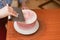 A lovely girl making a cake in a bakery. The girl smoothes the cream on the cake. White cake on a wooden table