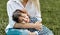 Lovely image of cute little child girl lying on her mother`s legs outside. Loving mother and daughter sitting on the green grass