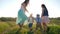 Lovely kids with girls teenagers lead round dance holding hands on green lawn near small river