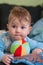 A lovely little baby lying on his stomach and plays with multi-colored soft ball