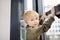 Lovely little boy sitting on the window near panoramic window and looking outside