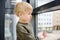 Lovely little boy sitting on the window near panoramic window and looking outside