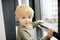 Lovely little boy sitting on the window near panoramic window and looking outside