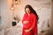 Lovely long-haired pregnant woman dressed in elegant pink negligee standing near the bed