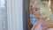 Lovely mature elderly couple is embracing, hugging and looking outside the window of their house