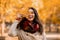 Lovely millennial woman smiling and closing her eye with yellow autumn leaf during her walk at park in fall