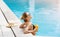 Lovely millennial woman with summertime cocktail relaxing in swimming pool, empty space