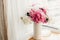 Lovely peony bouquet in sunny light on rustic wooden window sill. Stylish pink and white peonies in vase on wooden background.