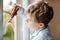 Lovely school kid boy in pajamas painting rainbow with colorful window color during pandemic coronavirus quarantine