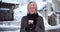 Lovely senior woman holding coffee cup standing on snowy street smiling