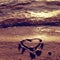 Lovely small heart sketched in salt sand at beach. Evening warm colors of sunset mirror in water level.