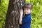 Lovely smiling little girl standing near big tree on green grass