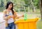 Lovely teen girl carry the bottles and throw green bottle to yellow bin in the garden