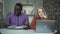 Lovely tired girl with a laptop and her African-American friend reading a book