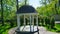 Lovely white gazebo. Trees and shrubs in the background. Fine garden with green grass