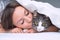 Lovely woman kissing her beautiful cat under the white blanket in the bed. Cat and owner together. Love for cats