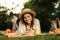 Lovely young girl in summer hat having a picnic at the park, laying on a grass,