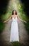 Lovely young lady wearing an elegant long white dress enjoying the beams of celestial light on her face in enchanted woods. Long