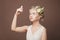 Lovely young woman blonde with healthy fair hair and white spring flowers and  butterfly on her head against brown wall background