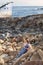 A lovely young woman gracefully elegantly sits on the stones waiting with an abandoned boat on the background