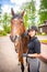 Lovely young woman wearing helmet stroking to her brown horse