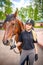 Lovely young woman wearing helmet stroking to her brown horse