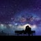 Lovers on bench in park. Couple silhouette at night. Milky Way at sky