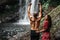 Lovers at the waterfall, rear view. Couple admiring a beautiful waterfall in Indonesia. Couple on vacation in Bali. Honeymoon trip