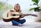 She loves learning new things. a little girl playing a guitar at home.