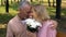Loving aged couple nuzzling during romantic date in park, flowers bunch present
