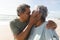 Loving biracial senior man kissing woman on lips at beach during sunny day