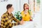 Loving boy and girl sitting in cafe, girl looking happy, taking selfie with flower, while boy doesn`t understand why she