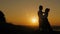 Loving couple - brave young man and beautiful girl stands on high hill at sunset and have hugs and kiss, silhouette