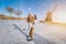 Loving couple having fun on ice in typical dutch landscape with windmill. Woman and man ice skating outdoors in sunny