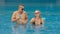 The loving couple hugs and kisses, drinking blue cocktail alcohol liquor in swimming pool at hotel outdoor. Portrait of