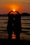 Loving couple make heart shape on beach with the sun set