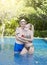 Loving couple in the pool in a garden with tropical trees. The man embraces the woman