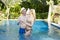 Loving couple in the pool in a garden with tropical trees. The man embraces the woman