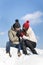 Loving couple sits on snow against blue sky. Guy warms hands of his beloved