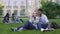 Loving couple of students sitting on lawn and watching video on smartphone