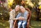 Loving elderly spouses resting in countryside, woman sitting in wicker chair, man embracing wife, copy space