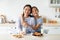 Loving korean mother and her daughter enjoying fresh homemade cookies, drinking milk, sitting in kitchen interior