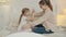 Loving mother giving gift box to child hugging daughter sitting on bed together