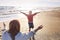 Loving mother stretched out arms to side of smiling daughter running towards her on sunny beach