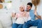 Loving pregnant arab couple having video call, waving hands to smartphone camera and smiling, resting on sofa
