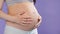 Loving pregnant woman holding her belly while posing in studio