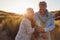 Loving Retired Couple Walking Arm In Arm Through Sand Dunes On Beach Vacation Against Flaring Sun