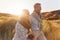 Loving Retired Couple Walking Arm In Arm Through Sand Dunes On Beach Vacation Against Flaring Sun