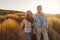 Loving Retired Couple Walking Arm In Arm Through Sand Dunes On Beach Vacation Against Flaring Sun